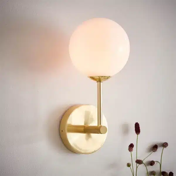 Brushed brass wall light with opal glass globe shade installed and lit